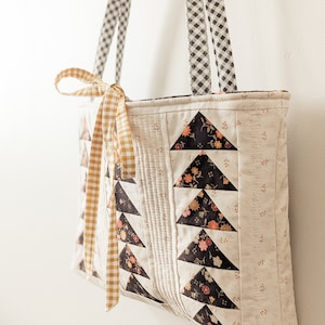 Peut inclure: Un sac cabas matelass&eacute; blanc avec des triangles en tissu &agrave; motifs floraux noirs. Le sac a deux anses en vichy noir et blanc et un ruban de nouage en vichy jaune.