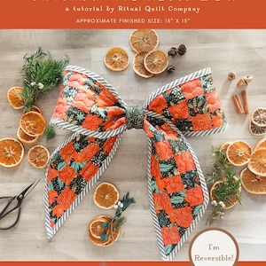 May include: A quilted Gingham Holiday Bow tutorial by Ritual Quilt Company. The bow is orange, black, and green with a striped border. Approximate finished size is 15" x 15". The image includes dried orange slices and greenery. The text says "I'm Reversible!"