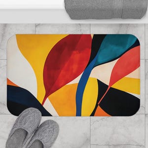 May include: A rectangular bath mat with an abstract design featuring large, stylized leaf shapes. The leaves are in shades of red, yellow, orange, blue, and black against a white background. Gray slippers are in the foreground.
