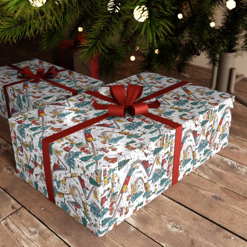 May include: Two rectangular gift boxes wrapped in white paper featuring a colorful illustrated pattern of winding train tracks, small houses, and evergreen trees, each finished with a wide, dark red satin ribbon tied in a bow.