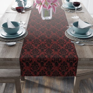 May include: A red and black damask table runner with a subtle distressed look. The runner is laid out on a wooden table with place settings on either side.