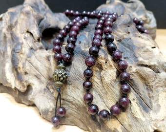 May include: A beaded necklace featuring deep red, round gemstones strung on a black cord. The necklace includes an ornate, antique-style metal pendant and matching gemstone beads at the end. The beads are approximately 8mm in diameter.