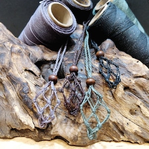 Può includere: Quattro collane in cordoncino macramé con perline di legno e una frangia annodata. Le collane sono esposte su un pezzo di legno di deriva.
