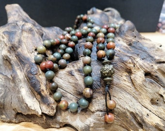 May include: A multi-colored stone mala necklace with a decorative metal bead. The necklace is made of green, brown, and red stones and is strung on a black cord.