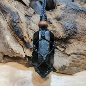 May include: Black obsidian crystal pendant with a black cord and wooden bead. The crystal is wrapped in a black macrame net.