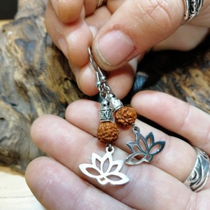May include: A pair of silver earrings with a lotus flower design and brown beads. The earrings are hanging from a person's hand.