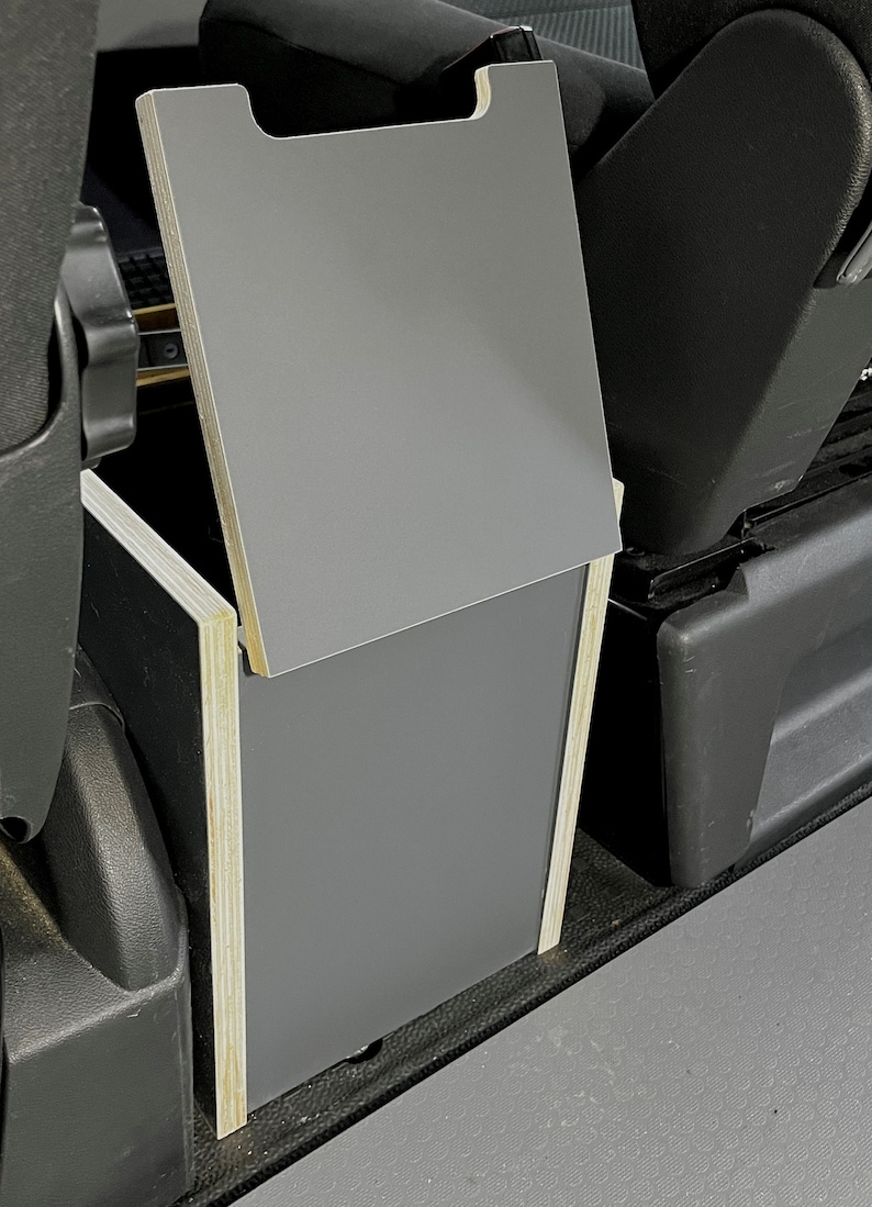 Puede incluir: Una caja de almacenamiento gris con una tapa con bisagras, hecha de madera y contrachapado, est&aacute; instalada en un veh&iacute;culo. La caja est&aacute; abierta y la tapa est&aacute; levantada.