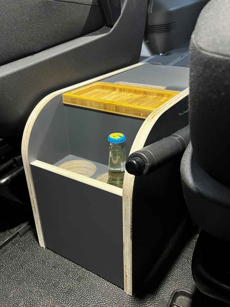 Puede incluir: Una caja de almacenamiento de madera gris con una bandeja de bamb&uacute; en la parte superior. La caja tiene dos portavasos y un espacio para una botella. La caja est&aacute; en un coche.