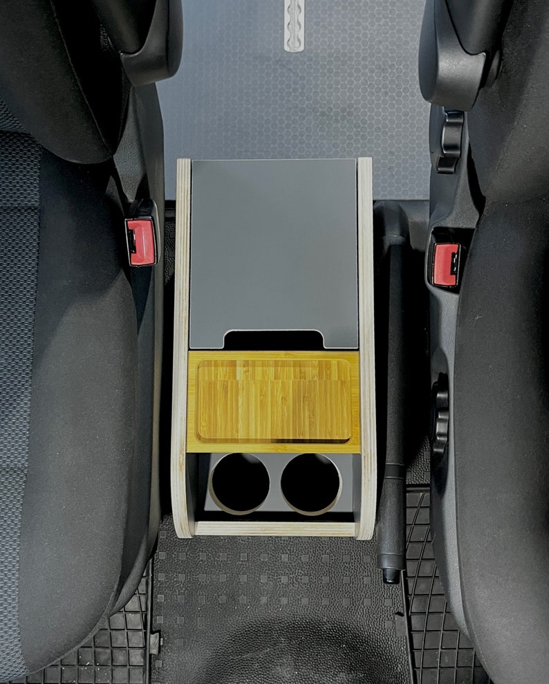 Puede incluir: Un organizador de consola de coche de madera con una parte superior gris, un estante de bamb&uacute; y dos portavasos. El organizador est&aacute; instalado entre dos asientos de coche.