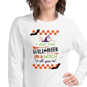 Könnte beinhalten: Weißes Langarm-T-Shirt mit einem schwarzen und violetten Hexenhut, Fledermäusen und dem Text "i don't need halloween im a witch all year" in Orange und Grün.