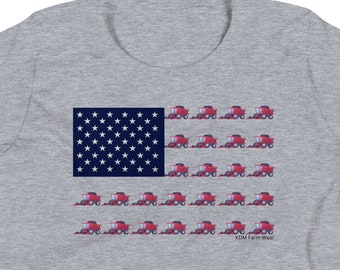 Puede incluir: Camiseta gris con un diseño de la bandera estadounidense. Las estrellas de la bandera son blancas y las franjas están representadas por cosechadoras rojas. El texto "KDM Farm Wear" está impreso en la parte inferior derecha del diseño.