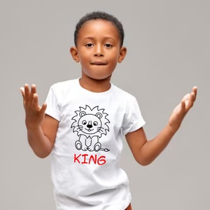 May include: White t-shirt with a black and white cartoon lion graphic and the word "KING" in red letters.