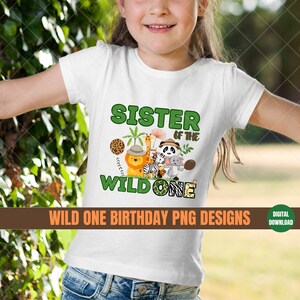 K&ouml;nnte beinhalten: Wei&szlig;es T-Shirt mit einer gr&uuml;nen und braunen Grafik, auf der "Schwester des Wilden" steht. Die Grafik zeigt einen L&ouml;wen, ein Zebra, eine Giraffe und andere Dschungeltiere.