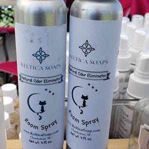 May include: Two silver spray bottles with white labels. The labels feature a black cat graphic and the text "Keltica Soaps Natural Odor Eliminator Room Spray www.KelticaSoap.com Charleston, SC Net wt. 4 Fl oz."
