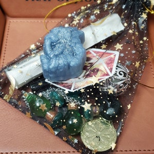 May include: A black mesh bag filled with various items, including a blue glitter soap, a silver charm, green glass beads, and a gold coin with a number 7 on it.