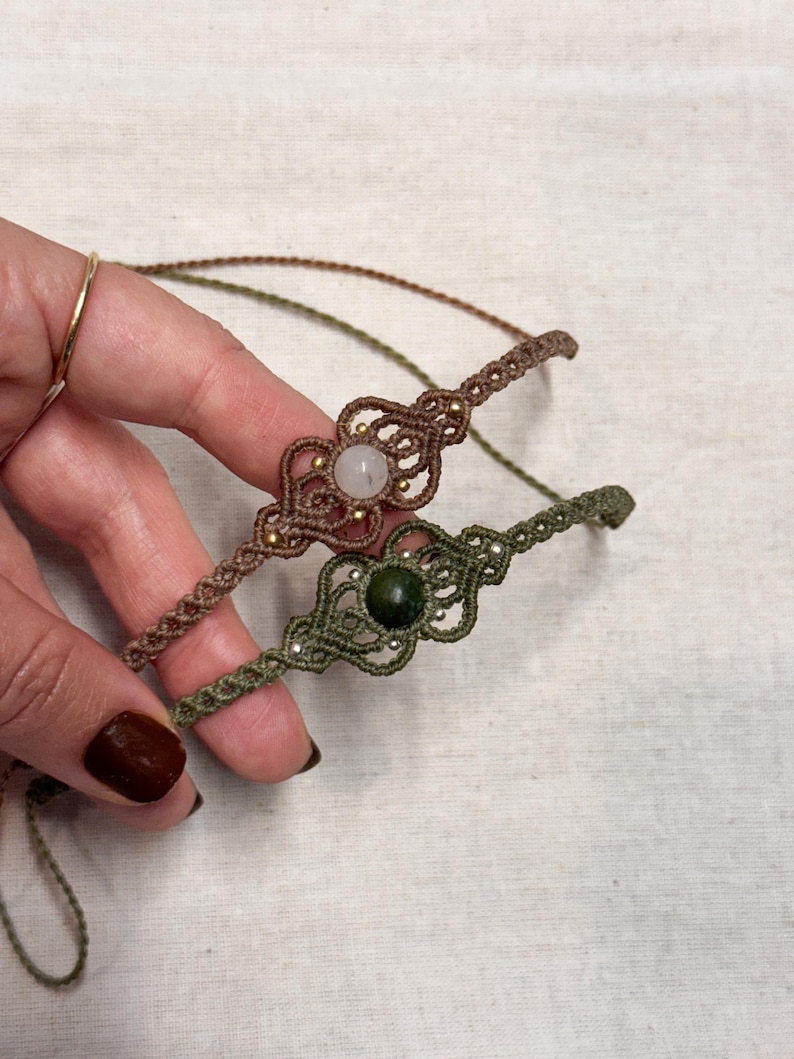 Puede incluir: Dos pulseras de macram&eacute;. Una es marr&oacute;n con una piedra clara y cuentas doradas, la otra es verde oliva con una piedra verde oscuro y cuentas plateadas. Las pulseras est&aacute;n hechas a mano y tienen intrincados patrones de nudos.