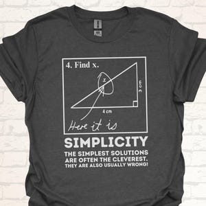 Könnte beinhalten: Ein dunkelgraues T-Shirt mit einer weißen Grafik eines rechtwinkligen Dreiecks mit dem Text "4. Find x." und "Here it is" unter dem Dreieck. Der Text "SIMPLICITY" ist in großen Buchstaben unter dem Dreieck geschrieben. Der Text "THE SIMPLEST SOLUTIONS ARE OFTEN THE CLEVEREST. THEY ARE ALSO USUALLY WRONG!" ist unter dem Wort "SIMPLICITY" geschrieben.