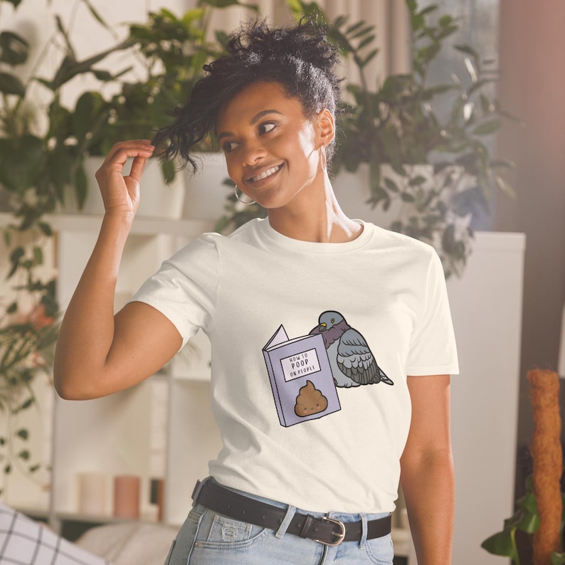 Unisex T-Shirt mit einer Taube die ein Buch liest auf dessen Einband How to poop on people steht.