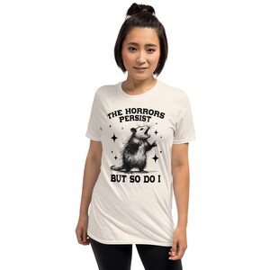 Unisex T-Shirt mit einem schreienden Opossum im Retro Stil und der Aufschrift: The Horrors Persist But so do I.