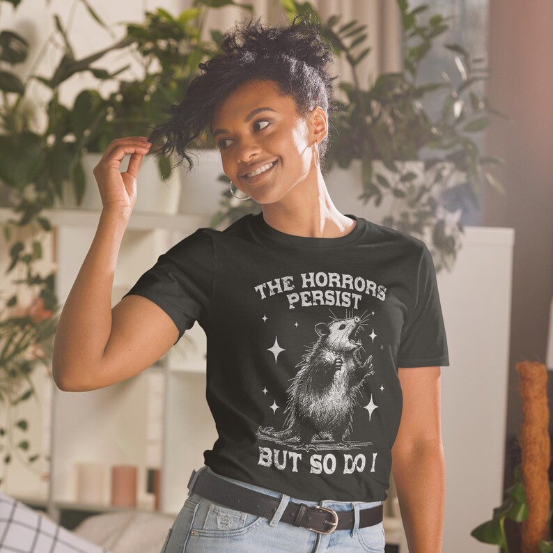 Unisex T-Shirt mit einem schreienden Opossum im Retro Stil und der Aufschrift: The Horrors Persist But so do I.