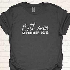 Può includere: Maglietta grigio scuro con testo bianco che dice "Nett sein ist auch keine Lösung".