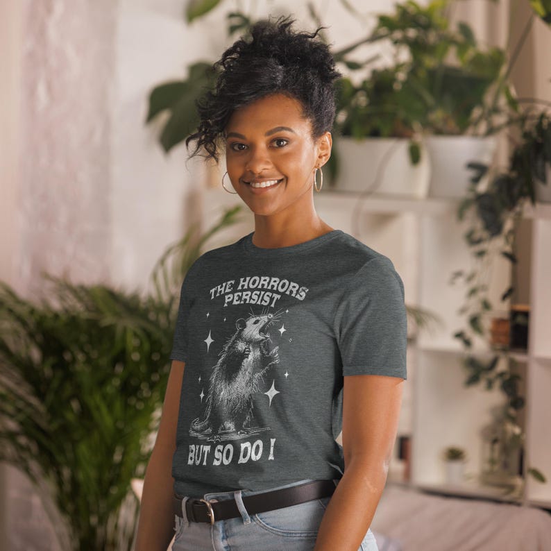 Unisex T-Shirt mit einem schreienden Opossum im Retro Stil und der Aufschrift: The Horrors Persist But so do I.