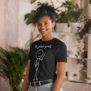 May include: Black t-shirt with the text "Bin jetzt gro&szlig;" and a stick figure design. The stick figure has the number 30 on its torso. The shirt is worn by a person with dark hair and hoop earrings.