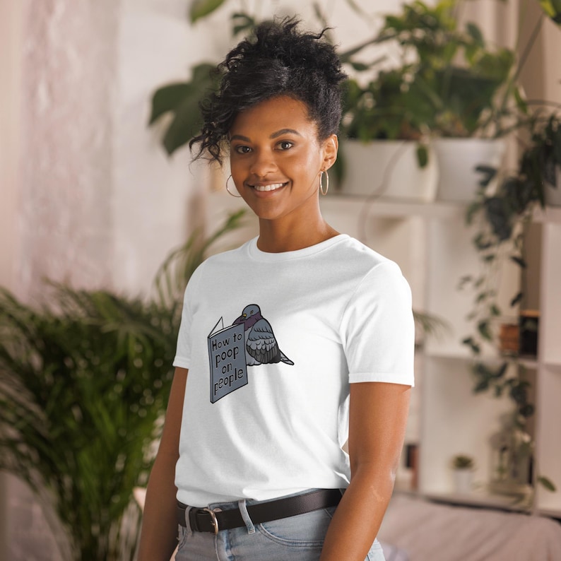 Unisex T-Shirt mit einer Taube die ein Buch liest auf dessen Einband How to poop on people steht.