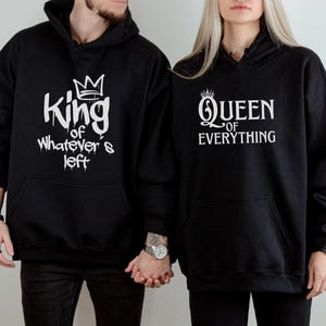 Puede incluir: Sudaderas con capucha negras con texto blanco. Una dice "King of Whatever's Left" con un gráfico de corona. La otra dice "Queen of Everything" con un gráfico de corona. Ambas tienen un bolsillo delantero.