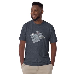 Unisex T-Shirt mit einer Taube die ein Buch liest auf dessen Einband How to poop on people steht.