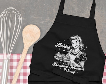 May include: Black apron with a white graphic of a woman holding cupcakes and the text "Baking Because Murder is Wrong."