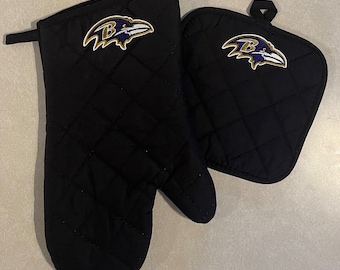 May include: A set of two black quilted oven mitts with a purple and gold Baltimore Ravens logo embroidered on each mitt.