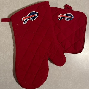 May include: Red quilted oven mitt and pot holder set. Each piece features a blue and white Buffalo Bills logo. The mitt has a loop for hanging. The set is made of a thick, heat-resistant material.