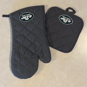 May include: A set of two black quilted oven mitts with the New York Jets logo in green and white. The logo features a football and the words "New York Jets".