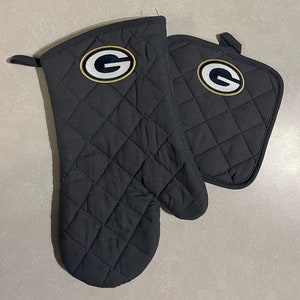 May include: A set of black quilted oven mitts with a green and gold embroidered "G" logo.