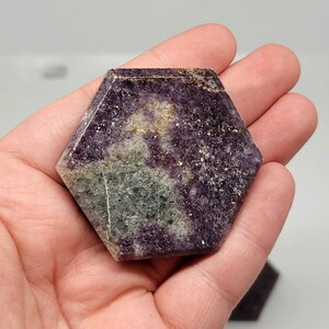 May include: A hexagonal shaped, polished lepidolite crystal with purple, grey, and white markings. The crystal is approximately 2 inches in diameter.