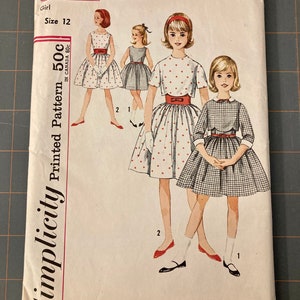 May include: Vintage Simplicity sewing pattern for a girl's dress. The pattern number is 4785 and the size is 12. The pattern is for a printed dress with a red bow and a plaid dress with a white collar.