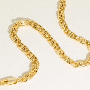 May include: A gold-toned chain necklace featuring a series of interlocking, oval-shaped links with a polished finish. The chain is arranged in a curved, serpentine pattern and includes a secure lobster claw clasp at one end for fastening.