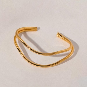 May include: A gold-toned double-band bangle bracelet with a wavy design.