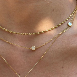 May include: Three gold necklaces with white round pendants. The top necklace is a twisted chain, the middle necklace is a delicate chain, and the bottom necklace has a larger pendant.