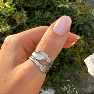 May include: A silver ring with a unique, organic design. The ring is made of two pieces of metal that are twisted together to create a flowing, wave-like shape.