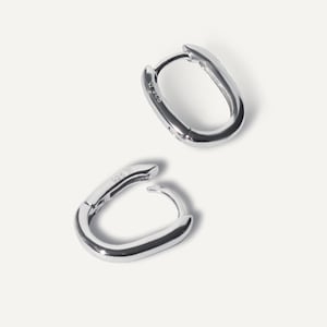 以下が含まれることがあります： 2つのシルバーカラーの楕円形フープピアス。ピアスは光沢のある反射性の金属製です。「925 16」の文字が片方のピアスに表示されています。ピアスは白い背景に表示されています。