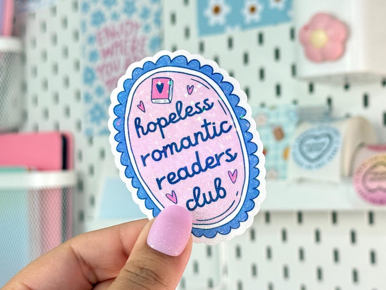 Peut inclure: Autocollant ovale rose avec une bordure bleue festonn&eacute;e. Il affiche l'inscription &laquo; hopeless romantic readers club &raquo; dans une police manuscrite, avec des illustrations de c&oelig;urs et de livres.