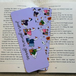May include: Two purple bookmarks with the text "just a gilmore goose" and illustrations of geese in various outfits. The bookmarks are set against the backdrop of an open book.