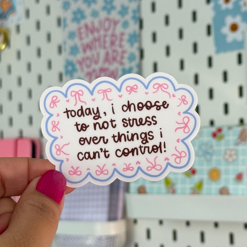 May include: A white sticker with a scalloped edge, featuring the text "today, I choose to not stress over things I can't control!" in brown. The border is light blue with pink bows and dots. The background includes other decorative stickers.