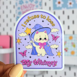May include: A die-cut sticker with a light purple background featuring a cream-colored cat wearing a blue wizard hat and cape with a pink bow. The cat holds a yellow star wand. Text reads I refuse to lose and My Whimsy with pink butterflies.