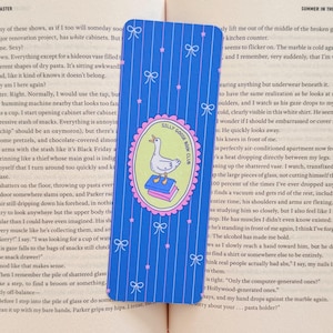May include: Blue bookmark with a pattern of vertical stripes, bows, and stars. The center features a circular emblem with a goose standing on books, with the text "Silly Goose Book Club".