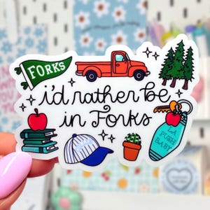 May include: A die-cut sticker featuring a red pickup truck, a green pennant labeled FORKS, a stack of books with an apple, a blue and white baseball cap, a cactus, and a keychain with the text LA PUSH BABY, surrounding the text i'd rather be in Forks.