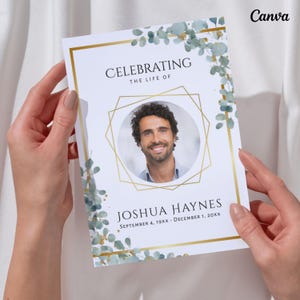 May include: A memorial card held by hands, featuring a photo of a man within a gold geometric frame. The card reads "Celebrating the Life of Joshua Haynes" with dates. Eucalyptus and gold accents decorate the edges.