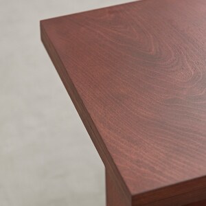 May include: Close-up of the top of a wooden table with a rich reddish-brown finish. The wood grain is visible and the surface is smooth.